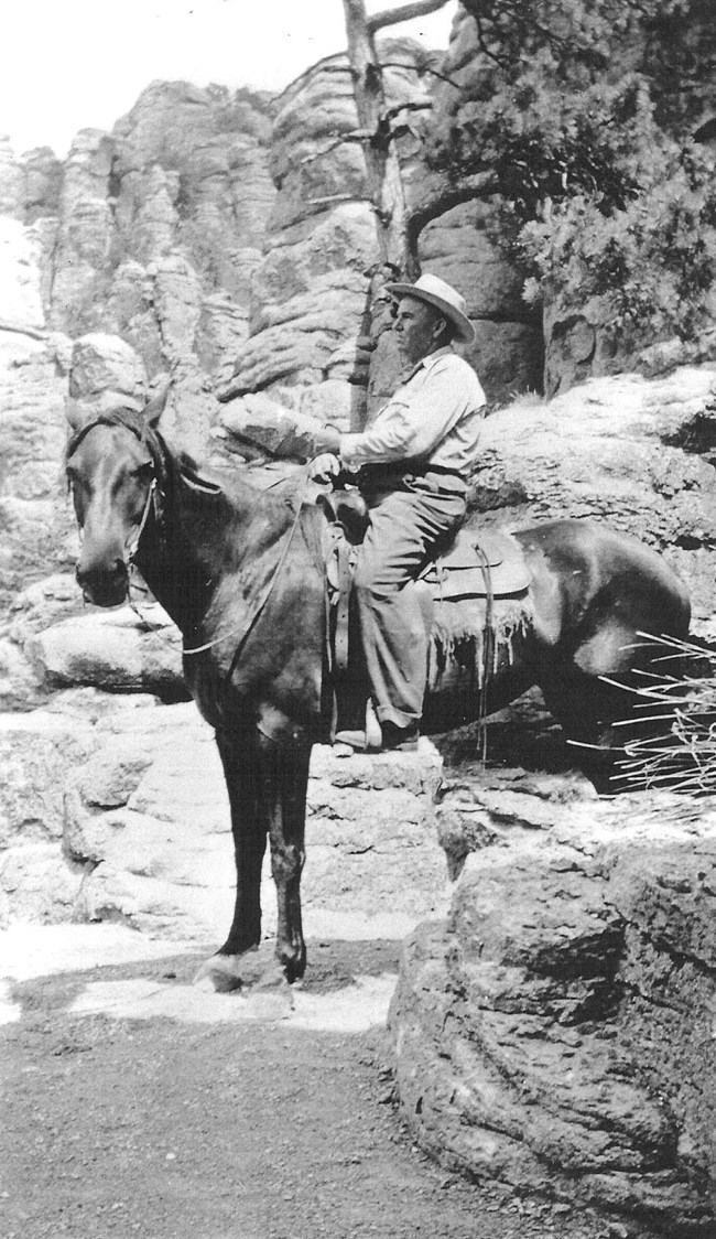 black and white photo of man on horse in front of rocks.