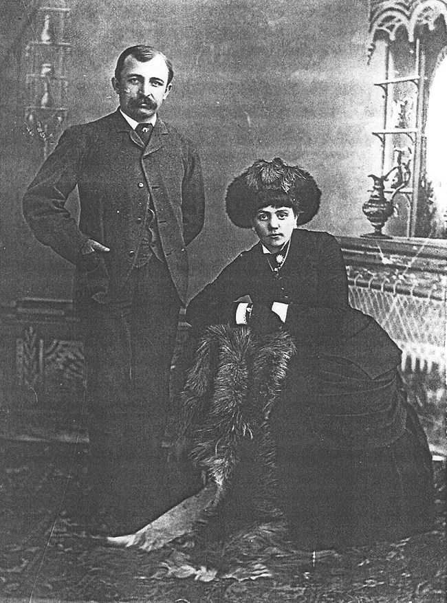 Black and white photo of seated woman and a man standing beside her.