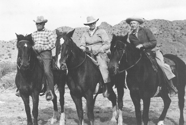 Three people on three horses in front of a hill.