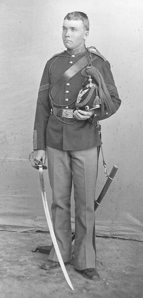 Black and white standing portrait of young man in military uniform holding a sword.