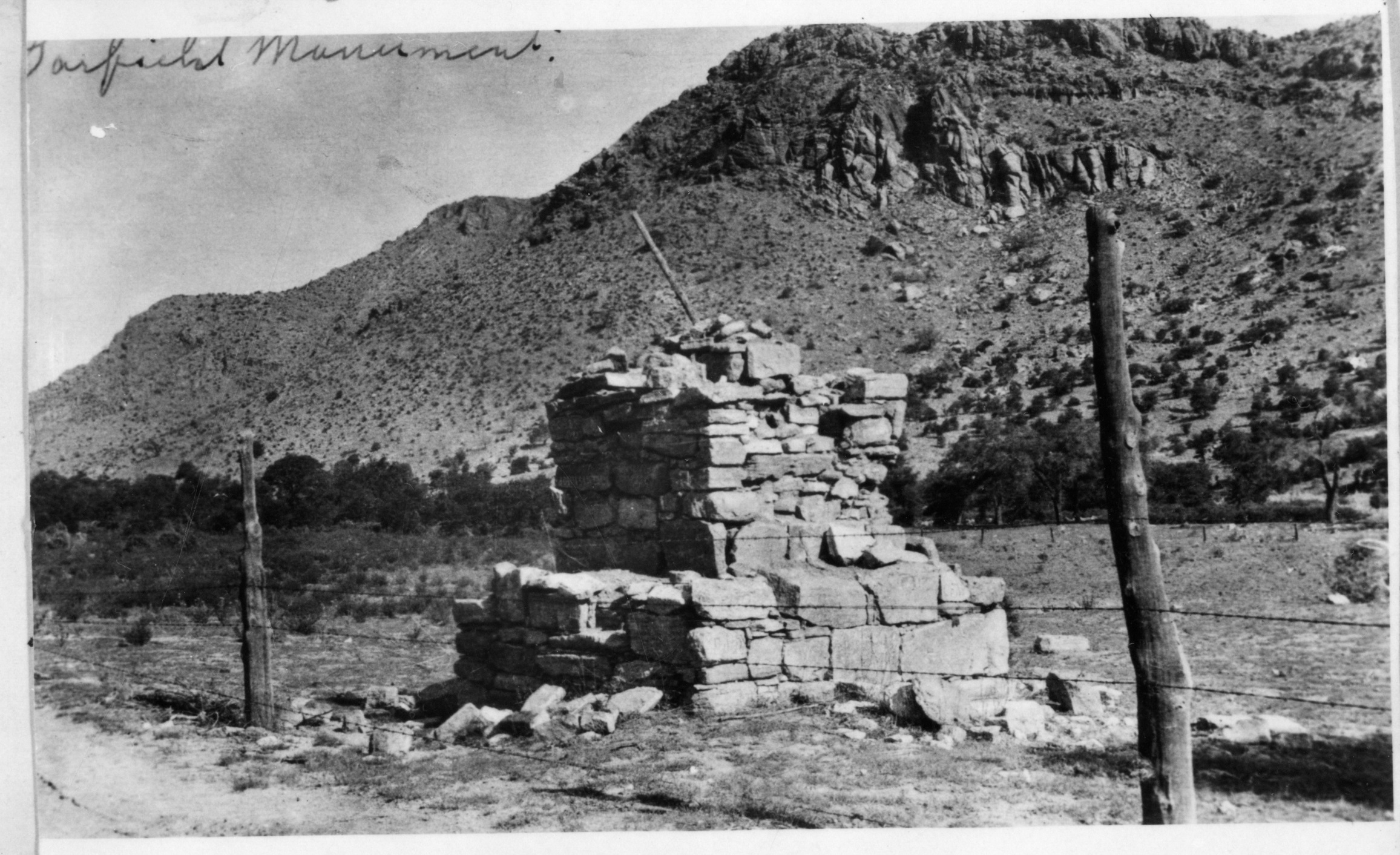 Three-tiered stone monument in field, behind a barbed wire fence.