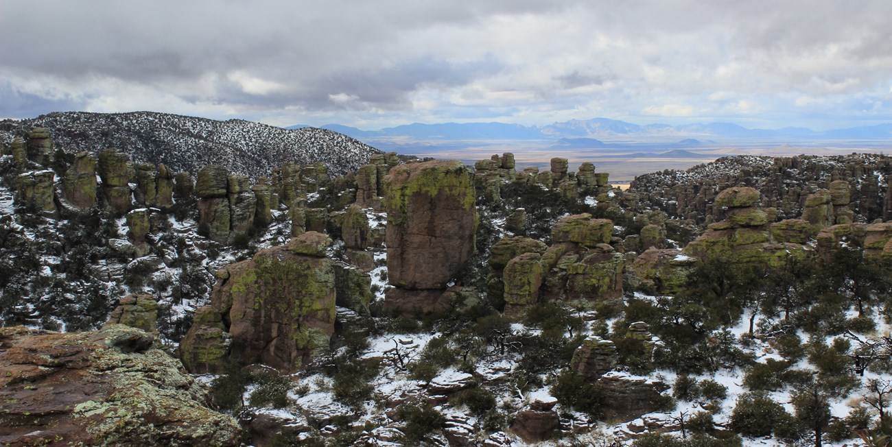 Photo of lots of rock formations covered in lichen, looking out towards a large valley.