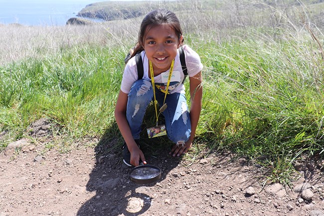 girl with magnifying glass in dirt