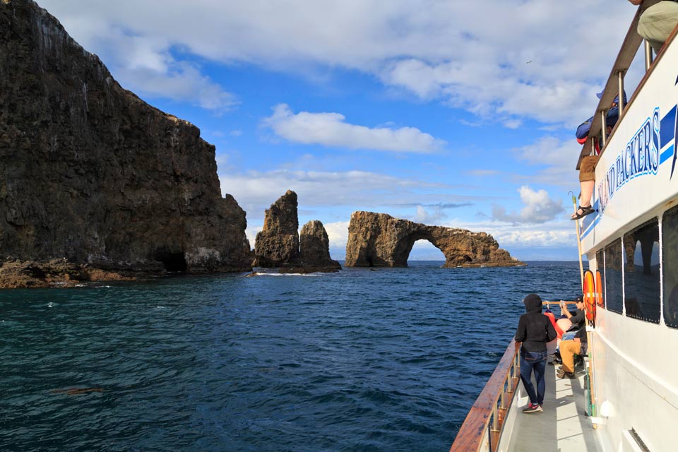 Boat on ocean looking at a rock shaped like an arch.
