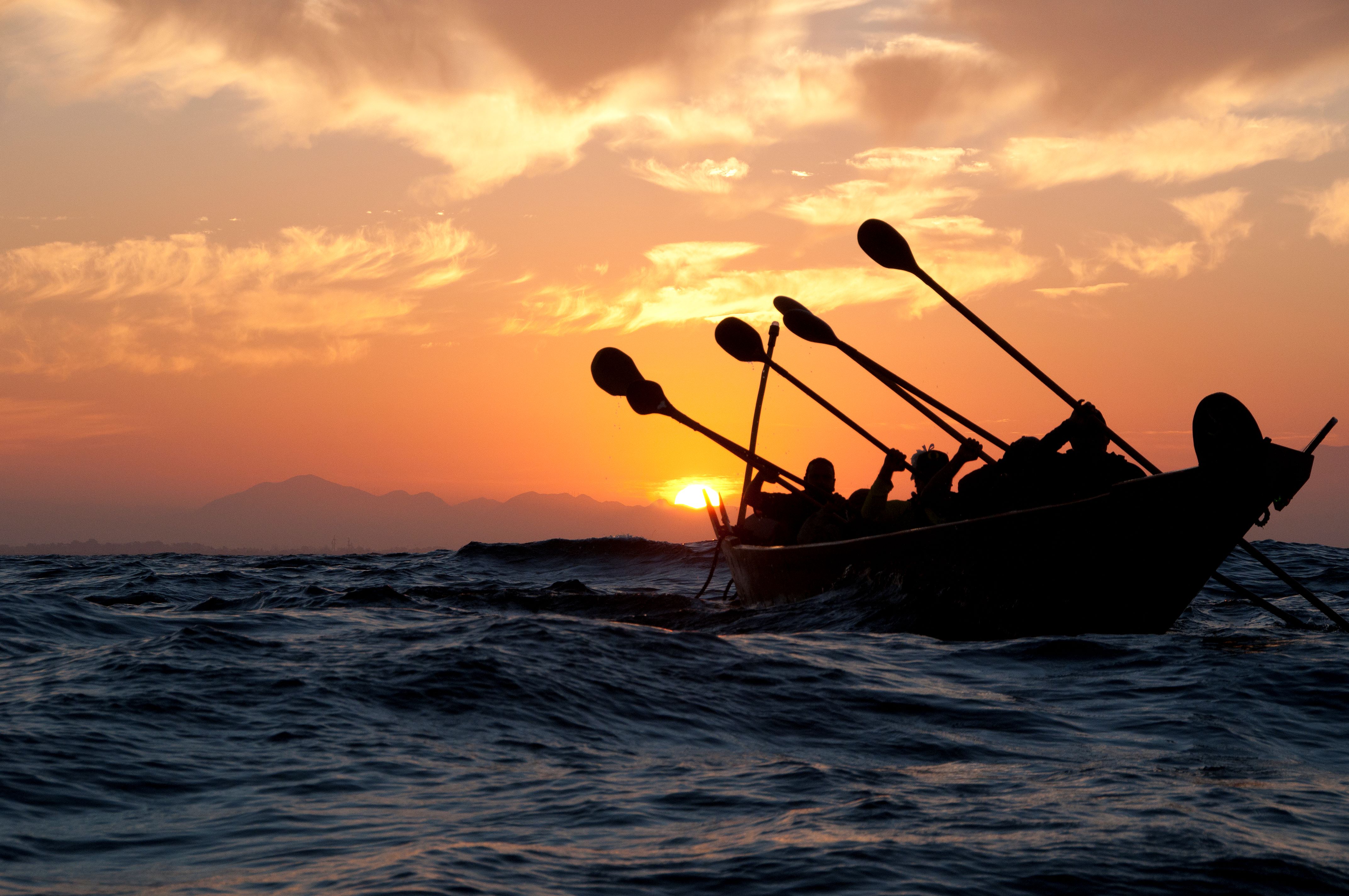 Paddlers in a canoe on the ocean at sunset.