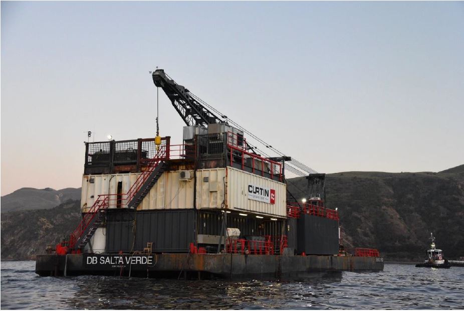 Large barge in ocean next to island.
