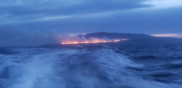 fire burning on island in distance. photo taken from boat.
