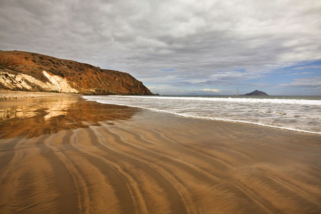 A shoreline with ripples in the sand under an overcast sky