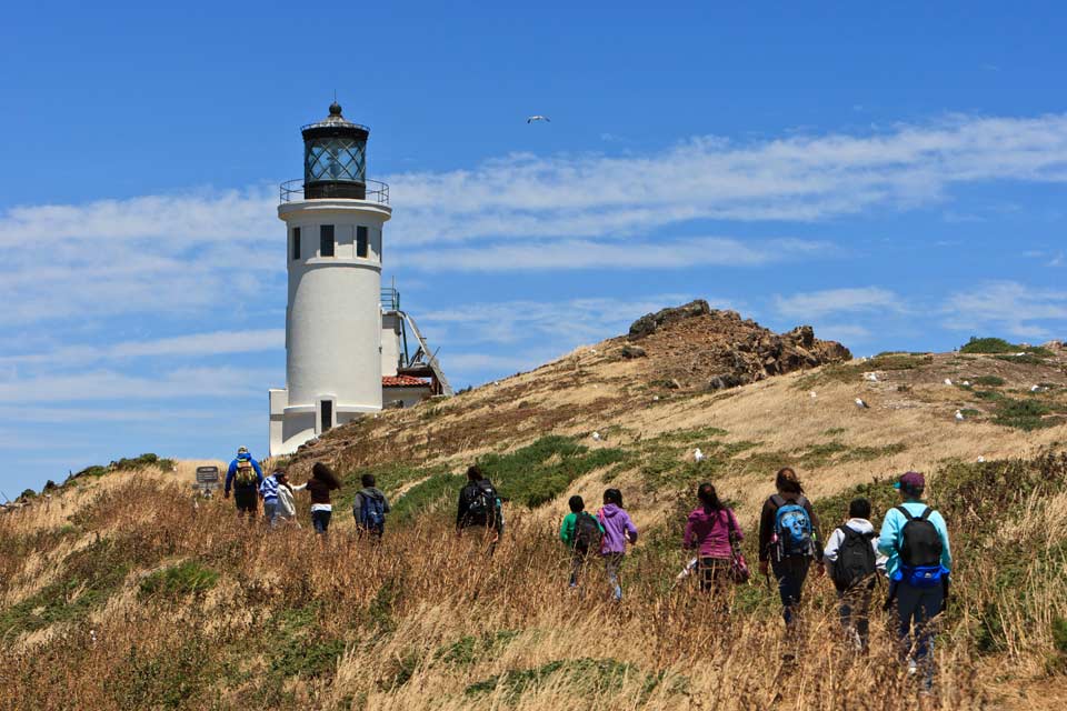 visitors walking towards a lighthouse on an ocean bluff