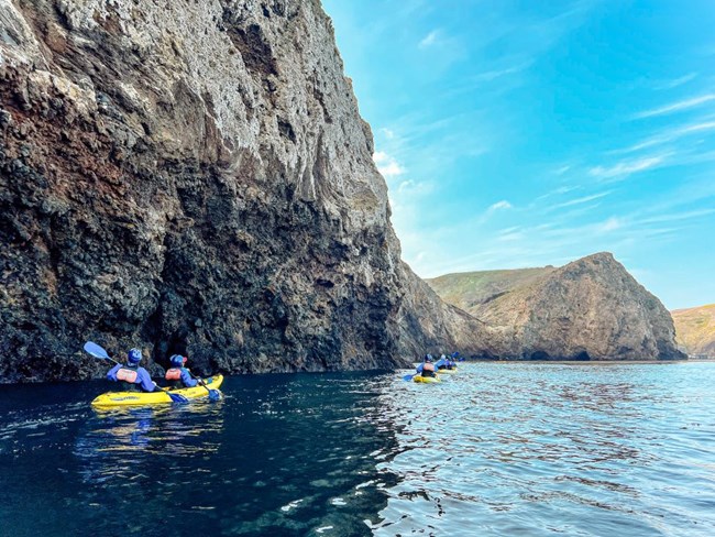 kayakers in ocean next to steep cliffs