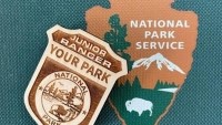 Wooden Junior Ranger badge on turquoise background with arrowhead NPS logo.