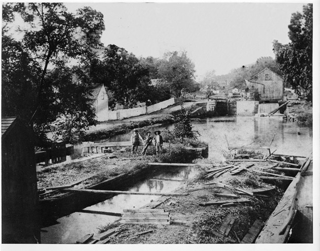 A historic photo shows two men and one boy resting against the beam that opens the lock gate.