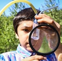 Boy examining a clear vial with a magnifying glass