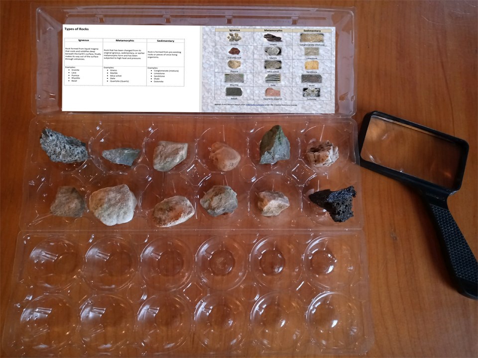 A collection of rocks set inside an egg carton with a magnifying glass next to the egg carton.