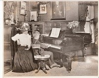 Theodore Edison as a boy playing the piano in Den at Glenmont, Miss Lucy Bogue at his side.