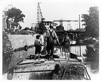 Historic image of a boy and girl holding onto their father's hands while on the canal boat.