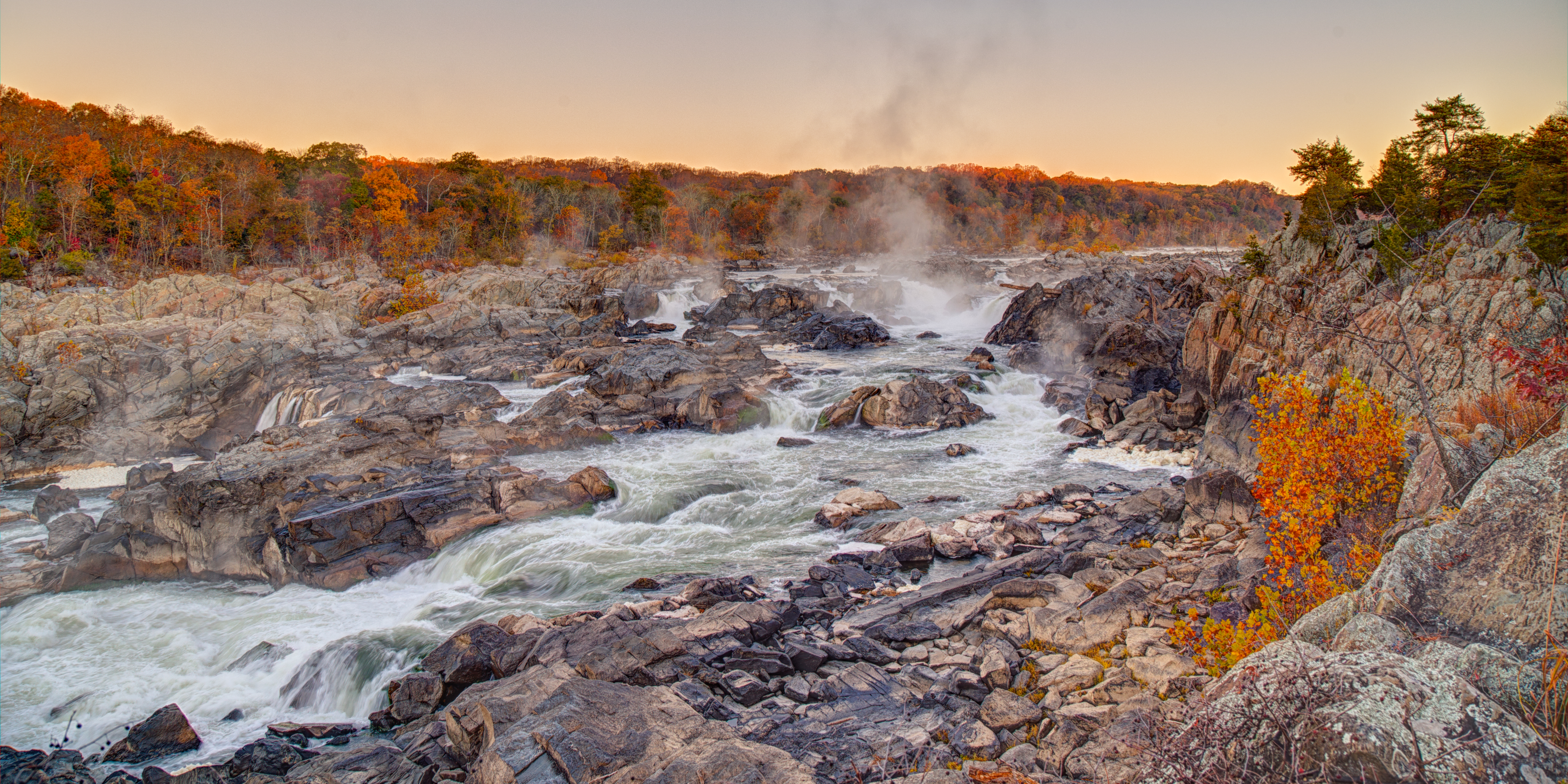 water flows over rocks with trees turning to fall