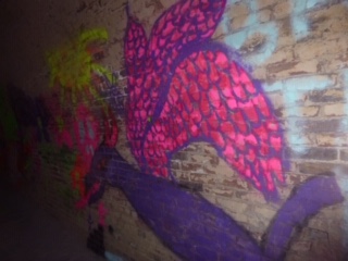 A pink and purple dragon spray painted on old bricks