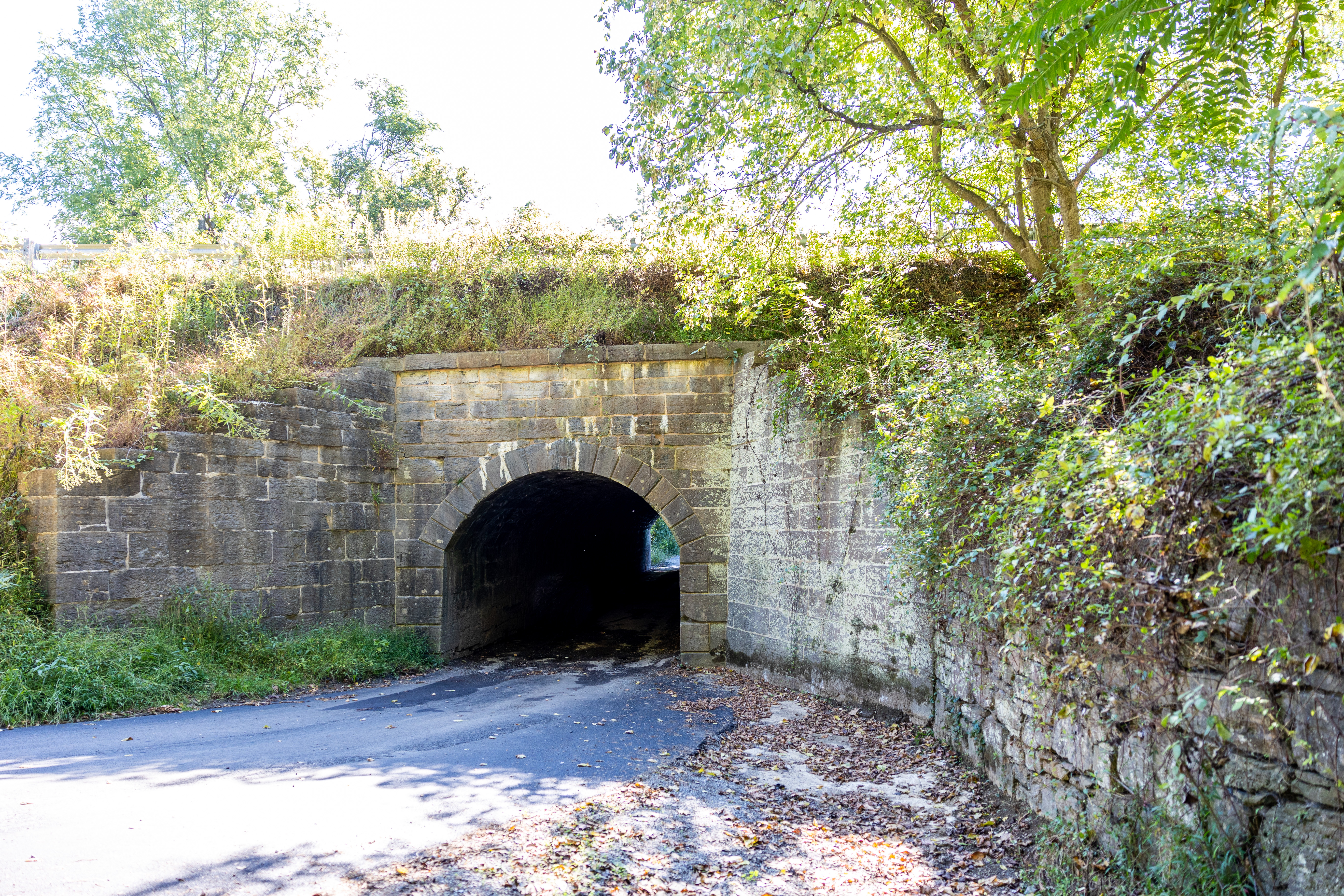 A gray stone masonry culvert with a paved road leading through it