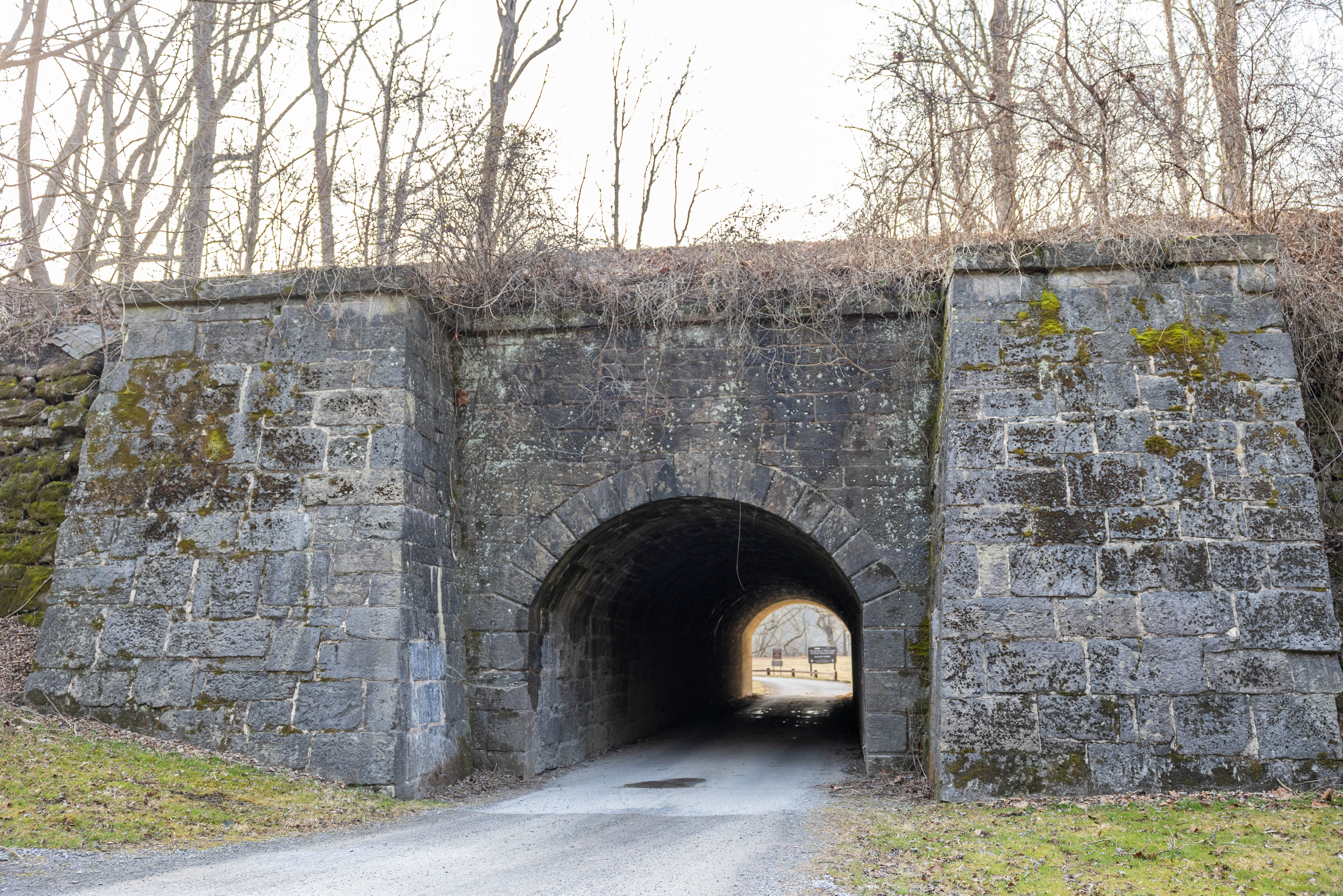 A gray stone masonry culvert with a gravel and paved road running through it