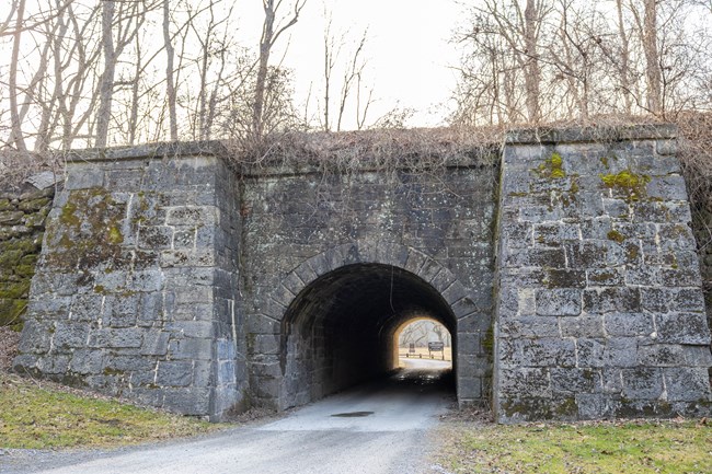 A gray stone masonry culvert with a gravel and paved road running through it