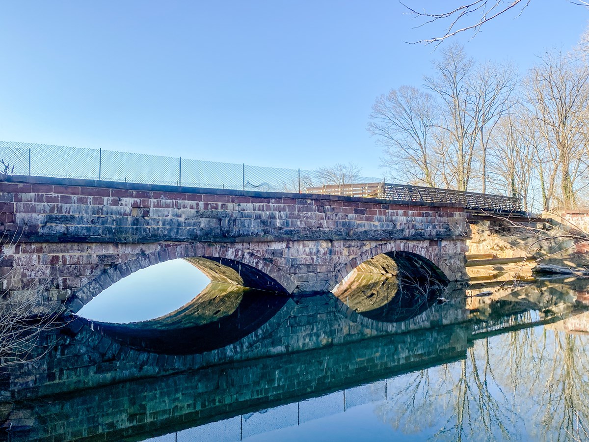 A stone aqueduct spans a creek on a sunny, clear day.