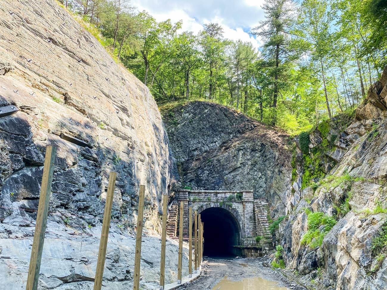 The Paw Paw Tunnel, a gray stone structure through a mountain, is shown in the background with a wooden boardwalk in the foreground