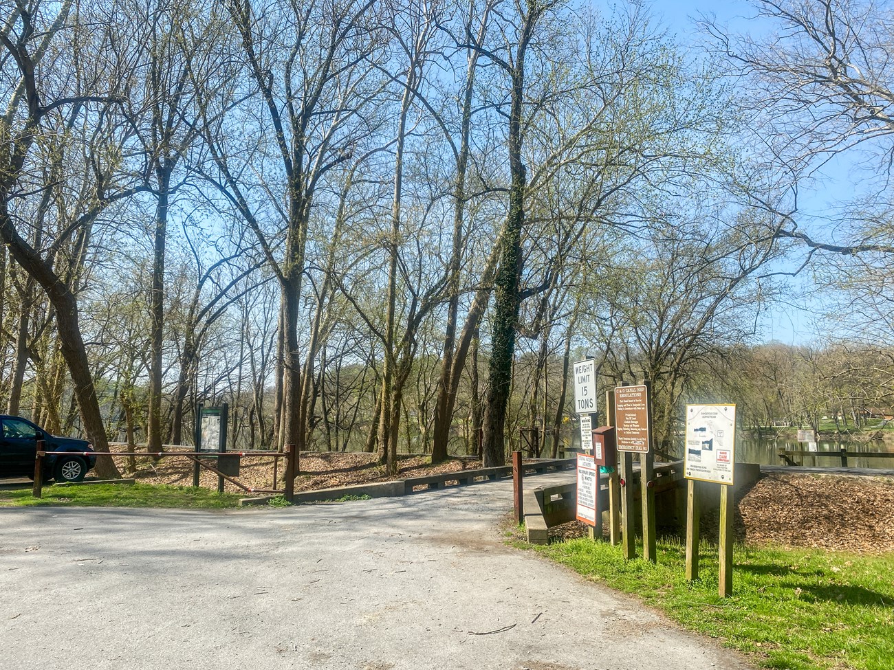 A vehicle bridge crosses the grassy canal with signage placed in the foreground