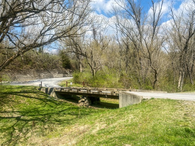 A concrete and wood vehicle bridge crosses the grassy canal prism