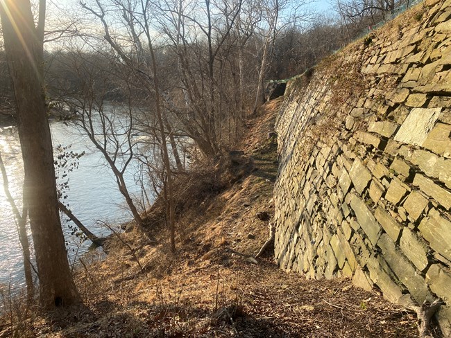 A dry-stacked stone wall runs along the right side of the image with the river parallel to it on the left side