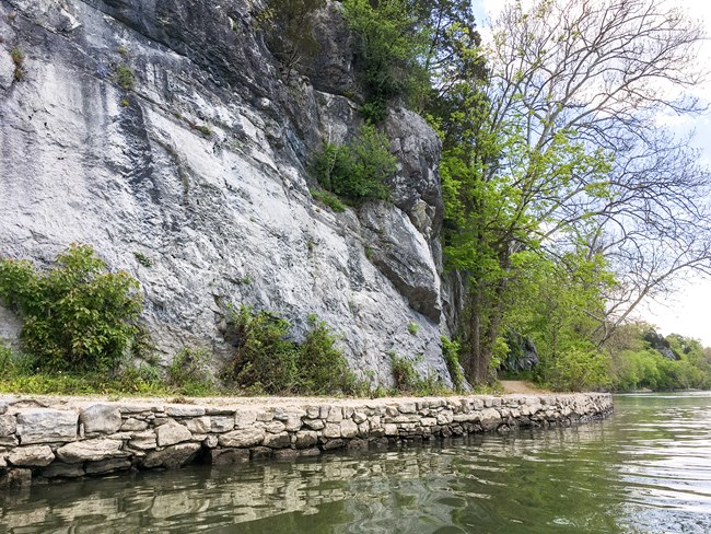 A pathway running between a river and a stone cliff