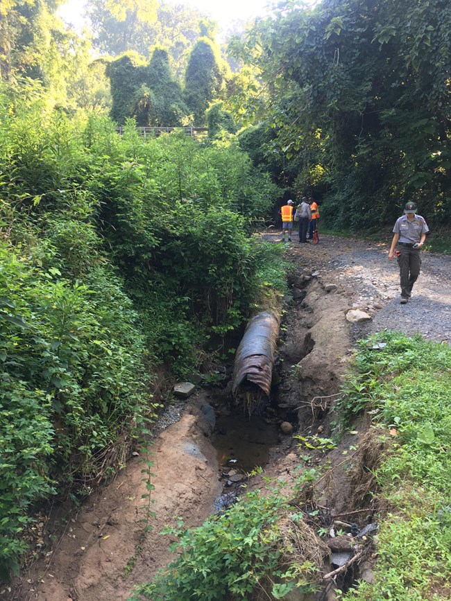 A water drainage pipe next to a roadway where severe erosion is present