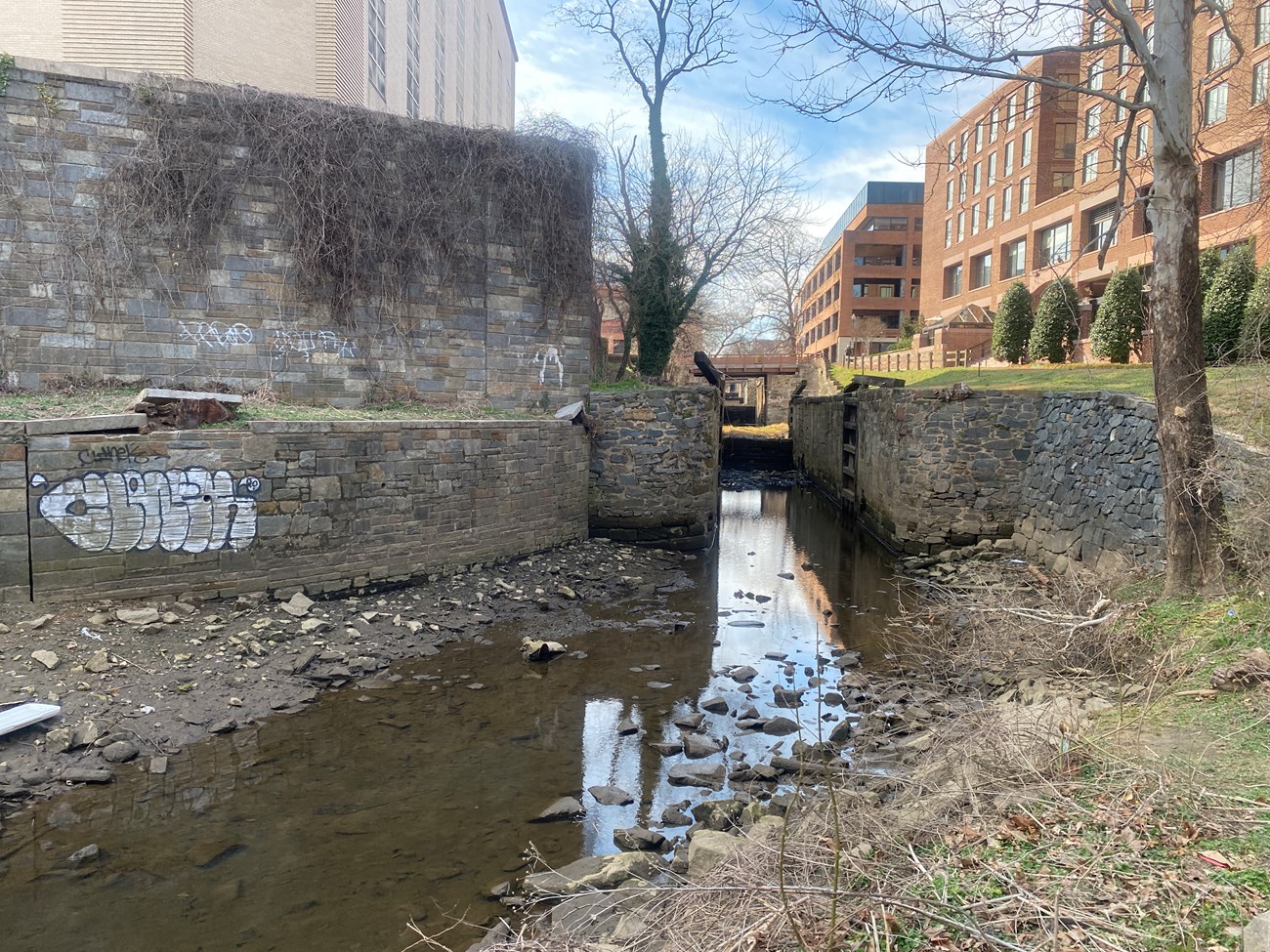 Photo of Lock 1 in Georgetown. There is shallow water in the canal, and masonry walls on either side of the canal.