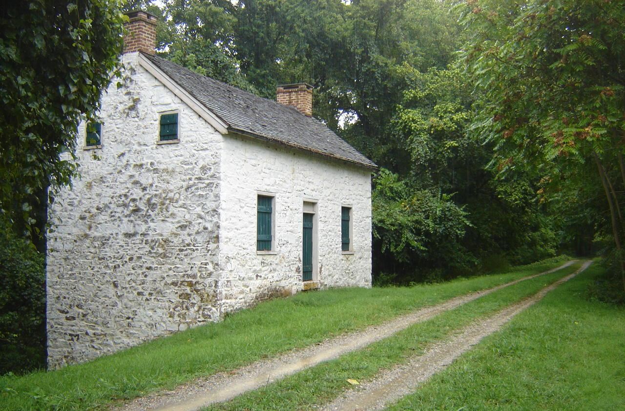 A lockhouse situated next to the towpath surrounded by trees.
