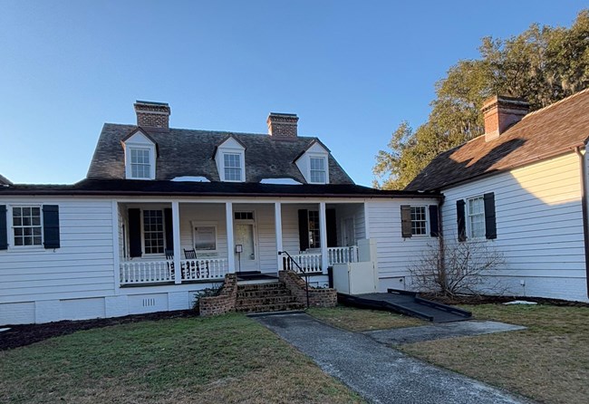 A one story house with white siding, a covered porch, and a sidewalk leading to it.