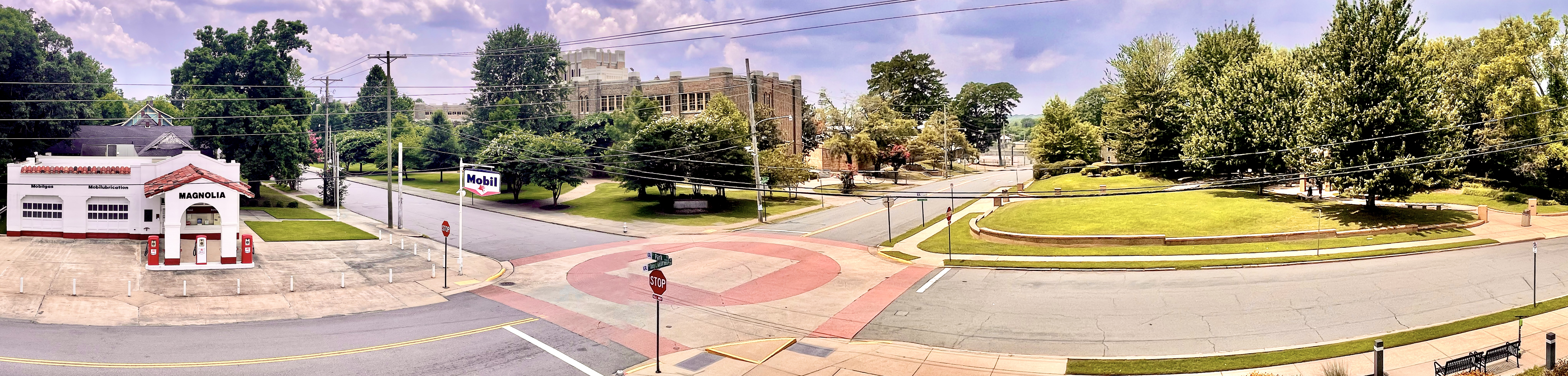 Panoramic view of an intersection showing the restored Magnolia gas station in the foreground and the historic Central High School building in the background.