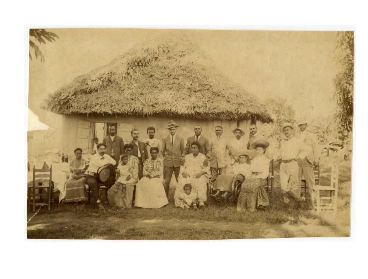 Charles Young standing in the center of the back row with others in Liberia. Courtesy of the National Afro-American Museum and Cultural Center, Wilberforce, Ohio. Black and white photo of Charles Young standing shoulder to shoulder with others looking directly at the camera. He is standing in the middle of the backrow of people. The first row is shoulder to shoulder sitting in chairs.