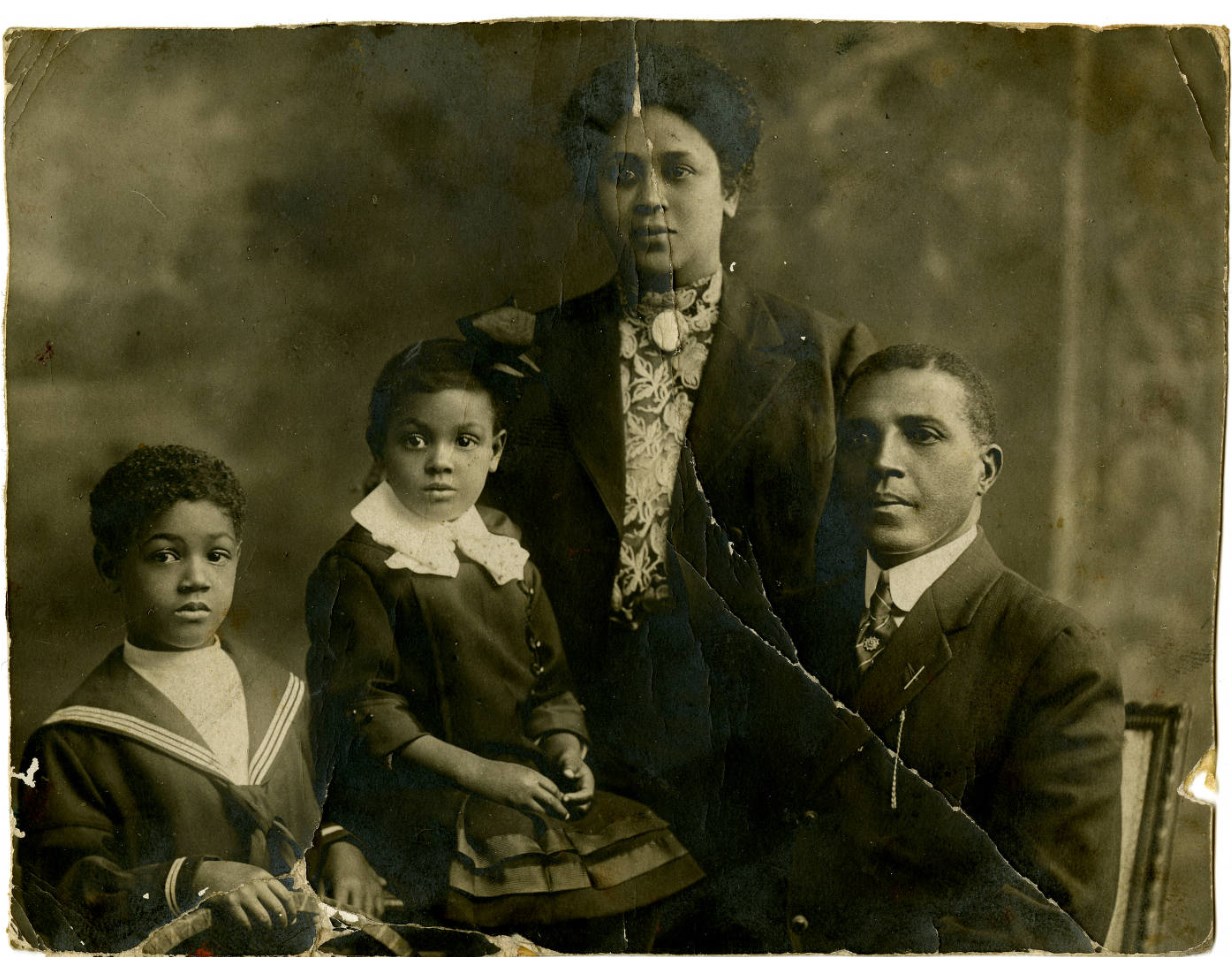 Black and white photo of African American family posing for a photograph. There are 4 people in the photo