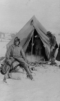 Charles Young sits on the plains in front of a tent in the winter.