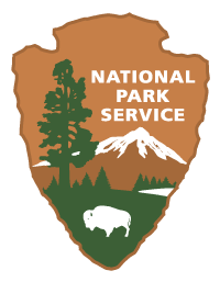 A tan arrowhead with trees, mountains, lake and bison with text reading National Park Service