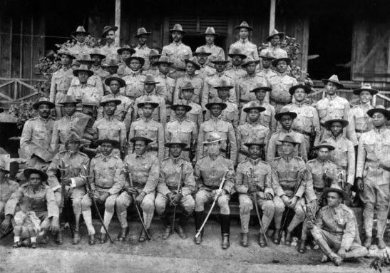 Several black Army soldiers standing and sitting while posing for a group portrait. Several black Army soldiers standing and sitting while posing for a group portrait.