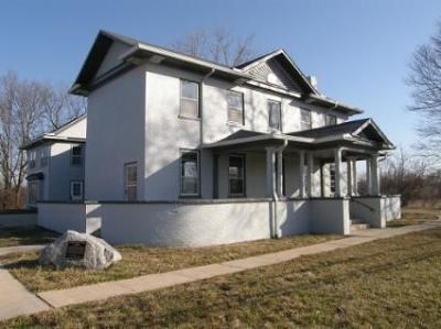 An oblique view of a large, two-story grey home with several windows on both levels and a large front porch.