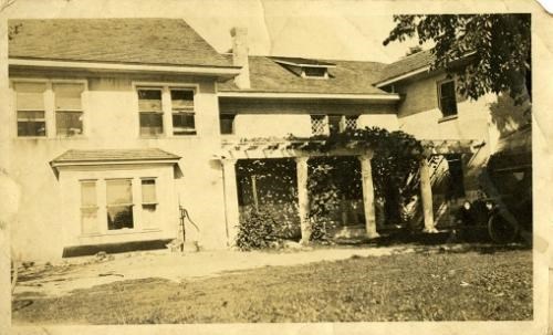 A large, two-story house with several windows and four pillars in the courtyard holding up a trellis.