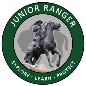 The park's Jr. Ranger logo showing a soldier on horseback holding a rifle surrounded by a green circle and a bison silhouette in the background.