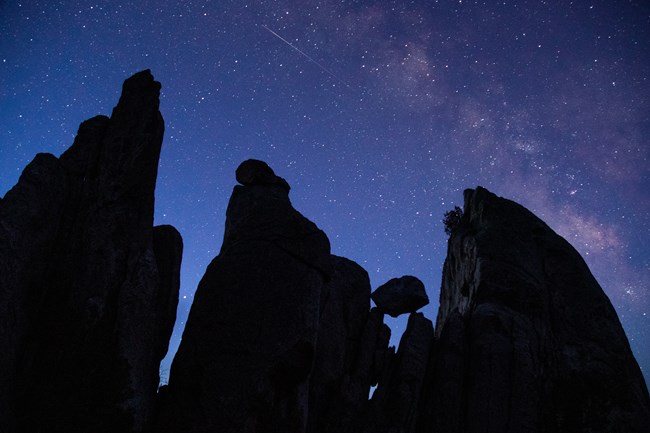 A boulder balances among towering granite formations with the milky way overhead.