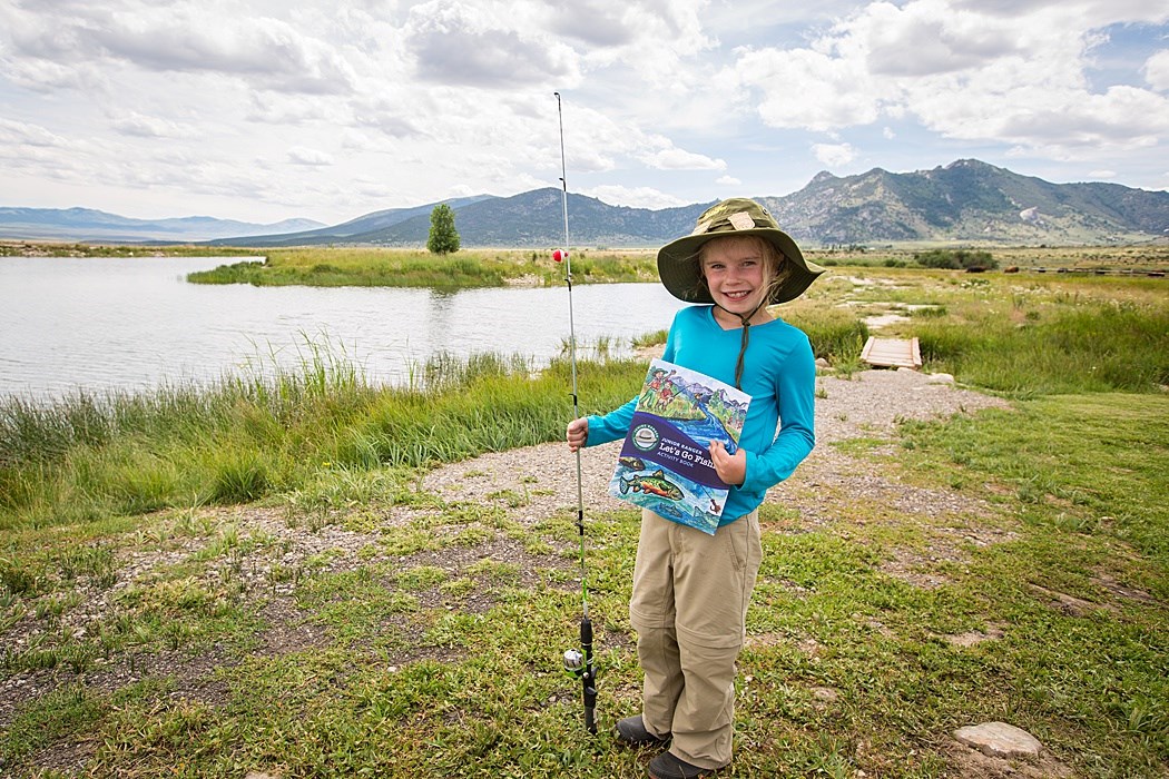 Girl in fishing hat holds fishing pole and new Junior Ranger Angler booklet