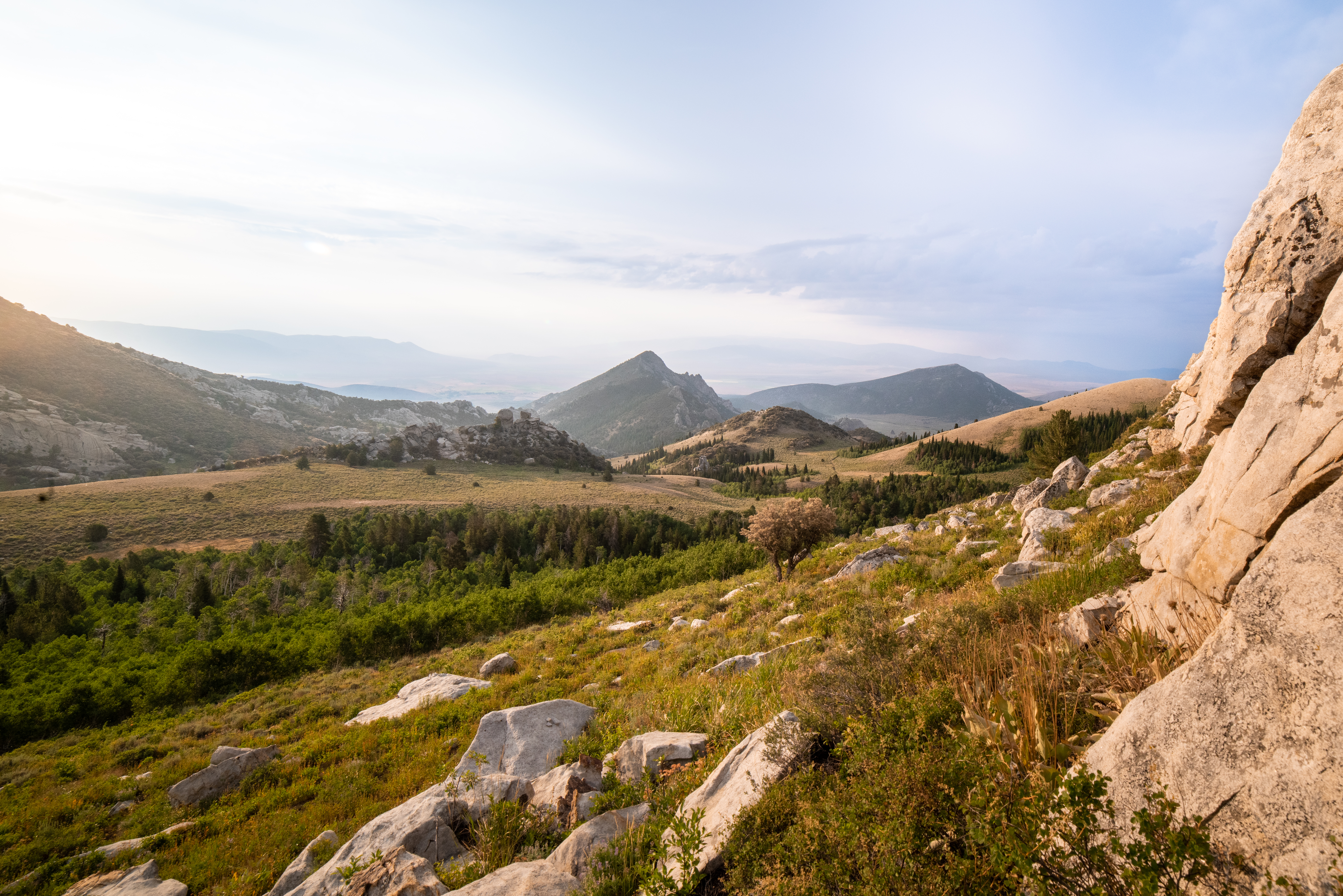 Photo is from the side of granite rock outcrop looking across a green lush canyon.