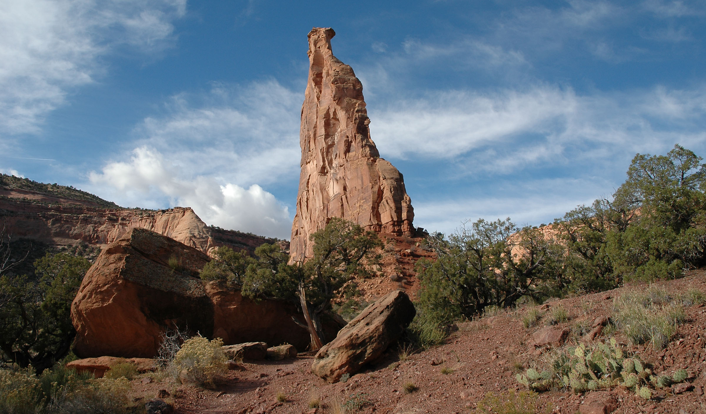 Independence Monument Pano Independence Monument stands out against the sky as the viewer looks up at it from near its base. There are rocks and foliage in the foreground.