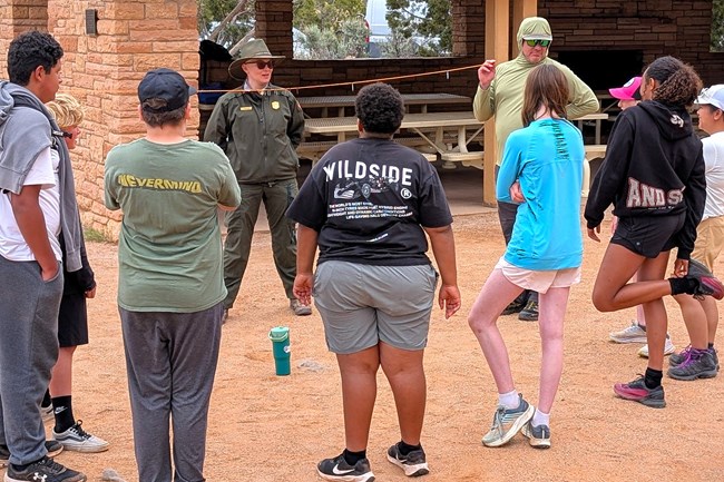 group of students stands around ranger and teacher holding a long string between them