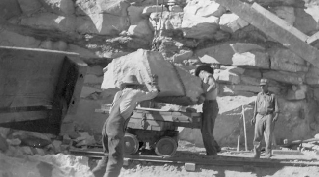 Two CCC workers using a pulley to lift a rock onto a cart